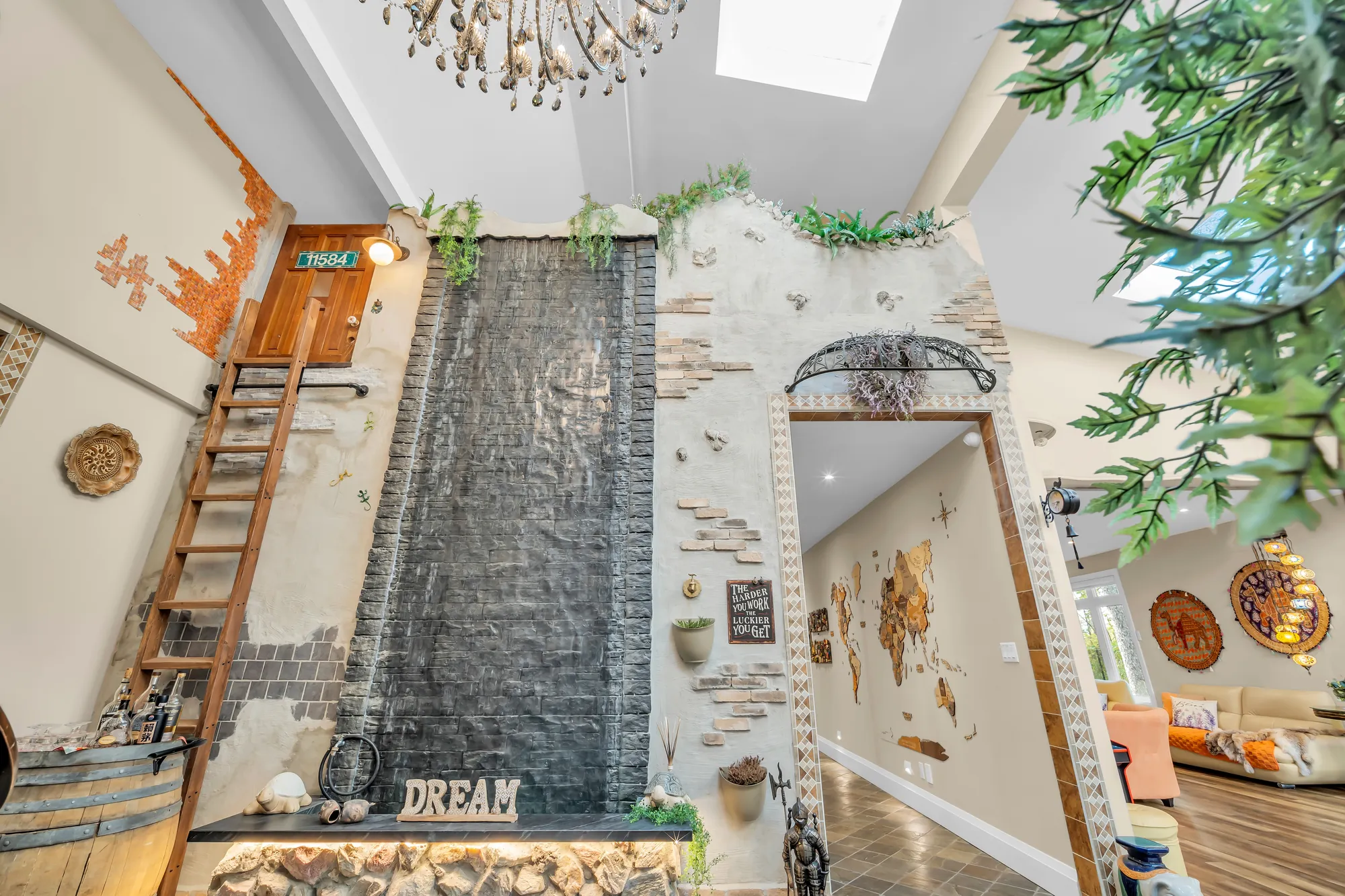 The water feature: water running down a dark stone wall above a bed of river stones, a wooden ladder, a wine barrel and a sign reading DREAM