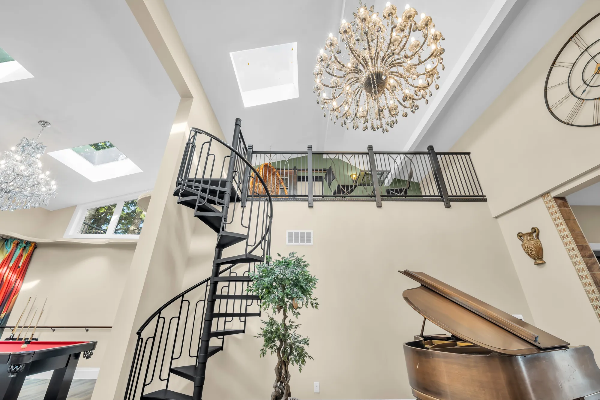 The black spiral stair rising to the loft, a crystal chandelier and skylights above, a pool table at the left