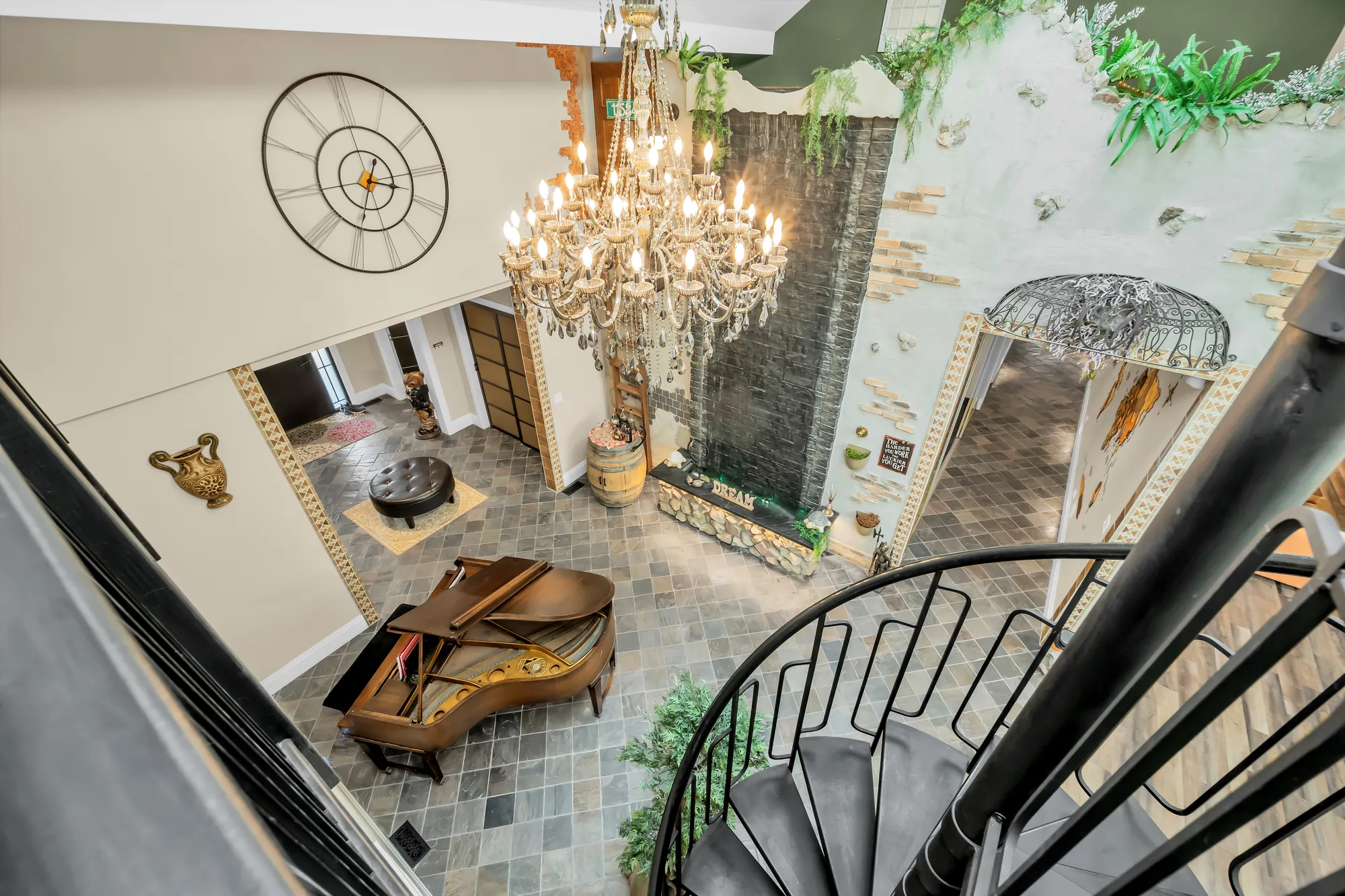 Looking down from the loft into the flex area: the piano, the spiral stair, a slate floor, a crystal chandelier, a wall clock