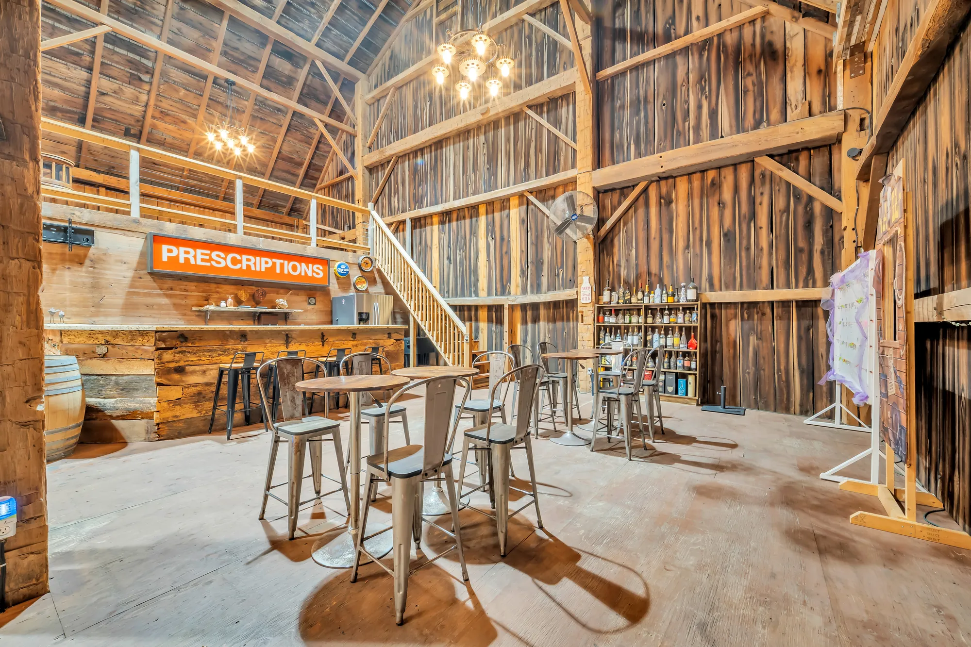 The bar: a counter of old wood, shelves of bottles, high tables and metal stools, a chandelier