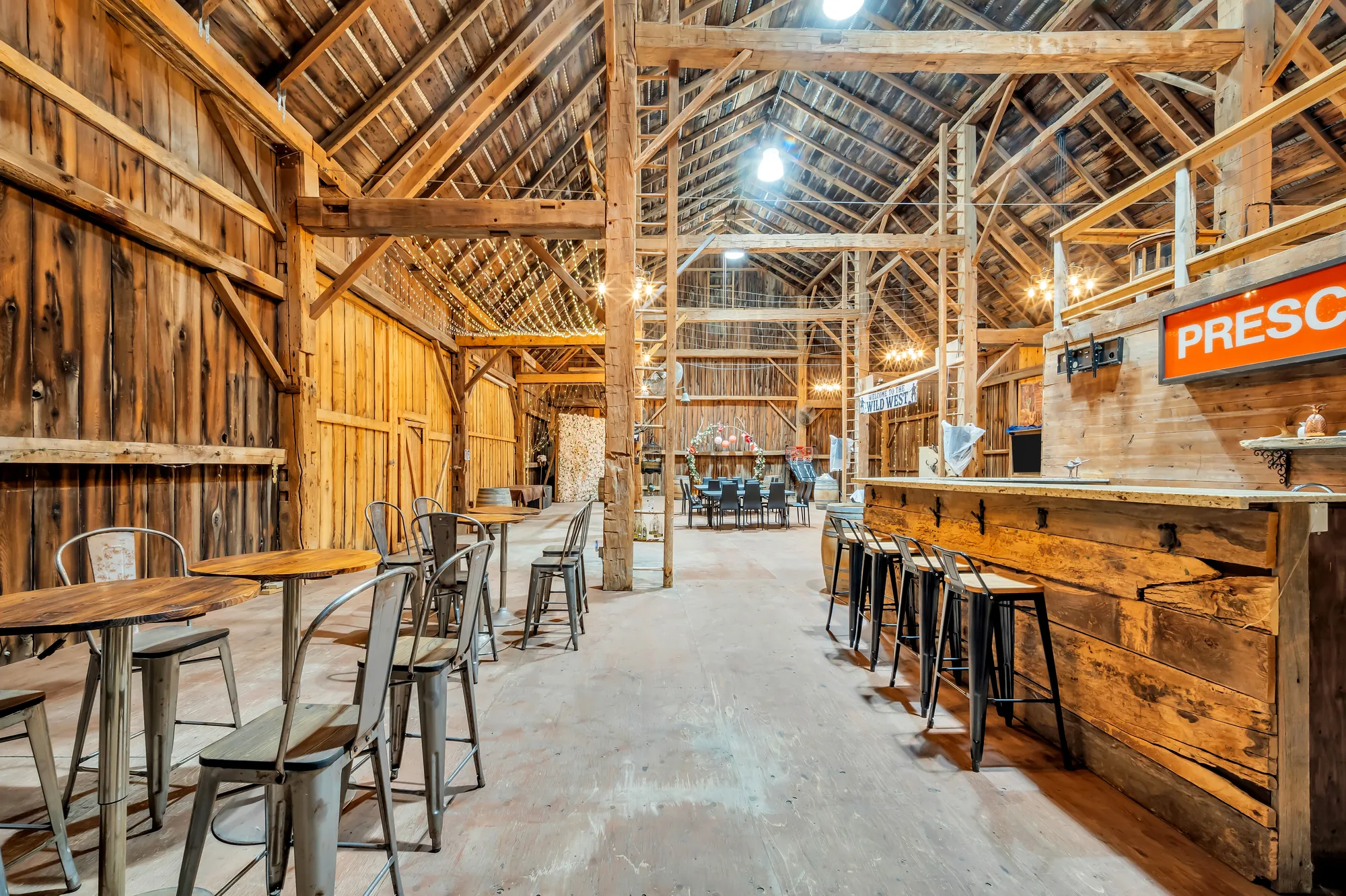 The bar counter with stools, high tables, the barn&rsquo;s timber frame and tables at the far end