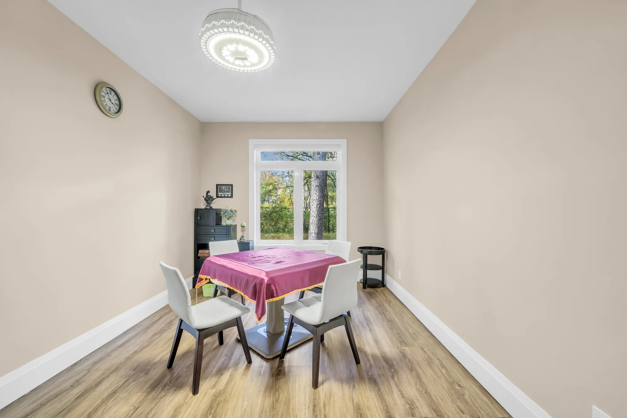 A bedroom set up as a sitting room: a small table with a purple cloth and four chairs, a window, a wall clock