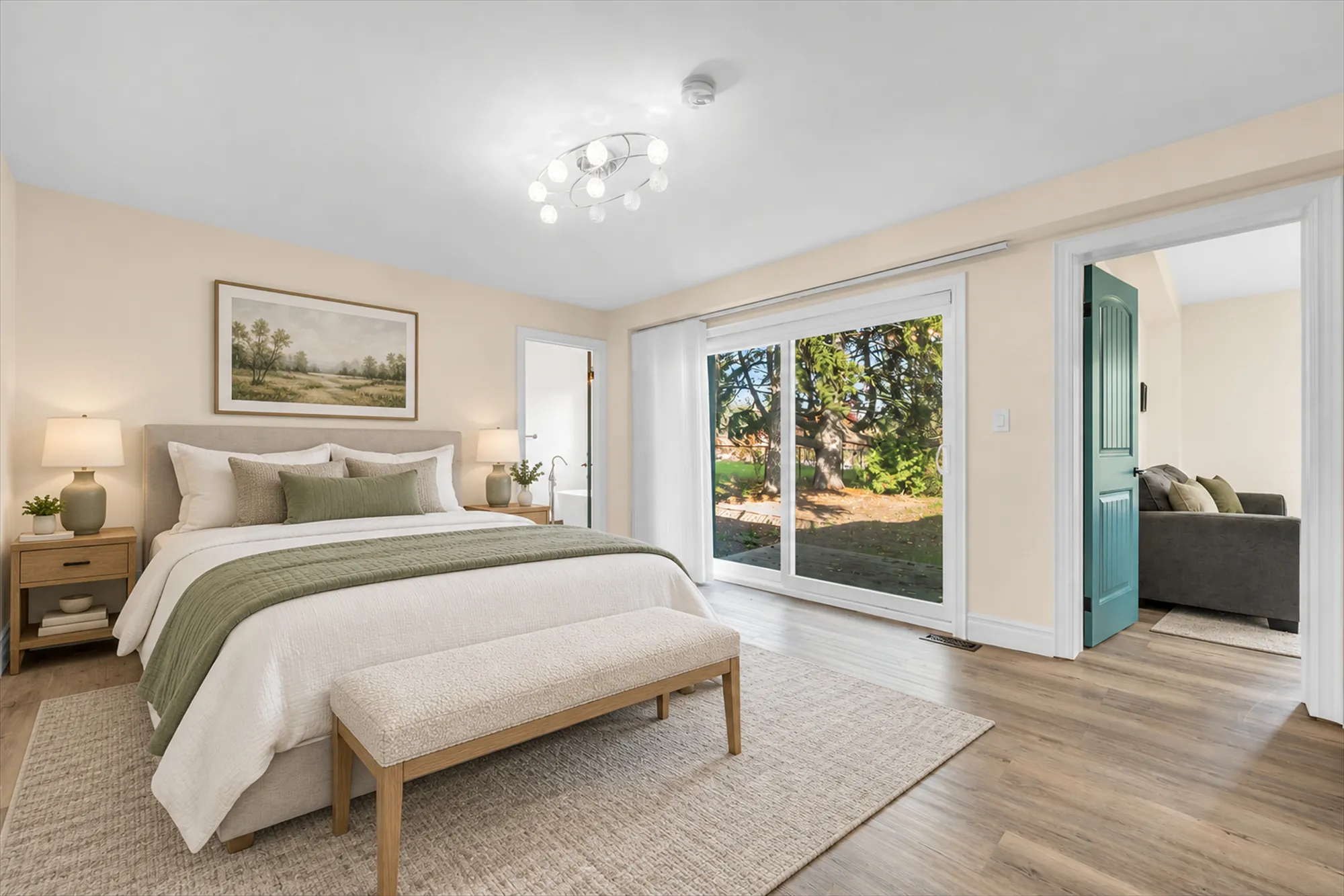 A bedroom with sliding glass doors to the outside, virtually staged: an upholstered bed with a green throw, a bench, a rug, oak night tables and lamps, a landscape print; a teal door open to the living room
