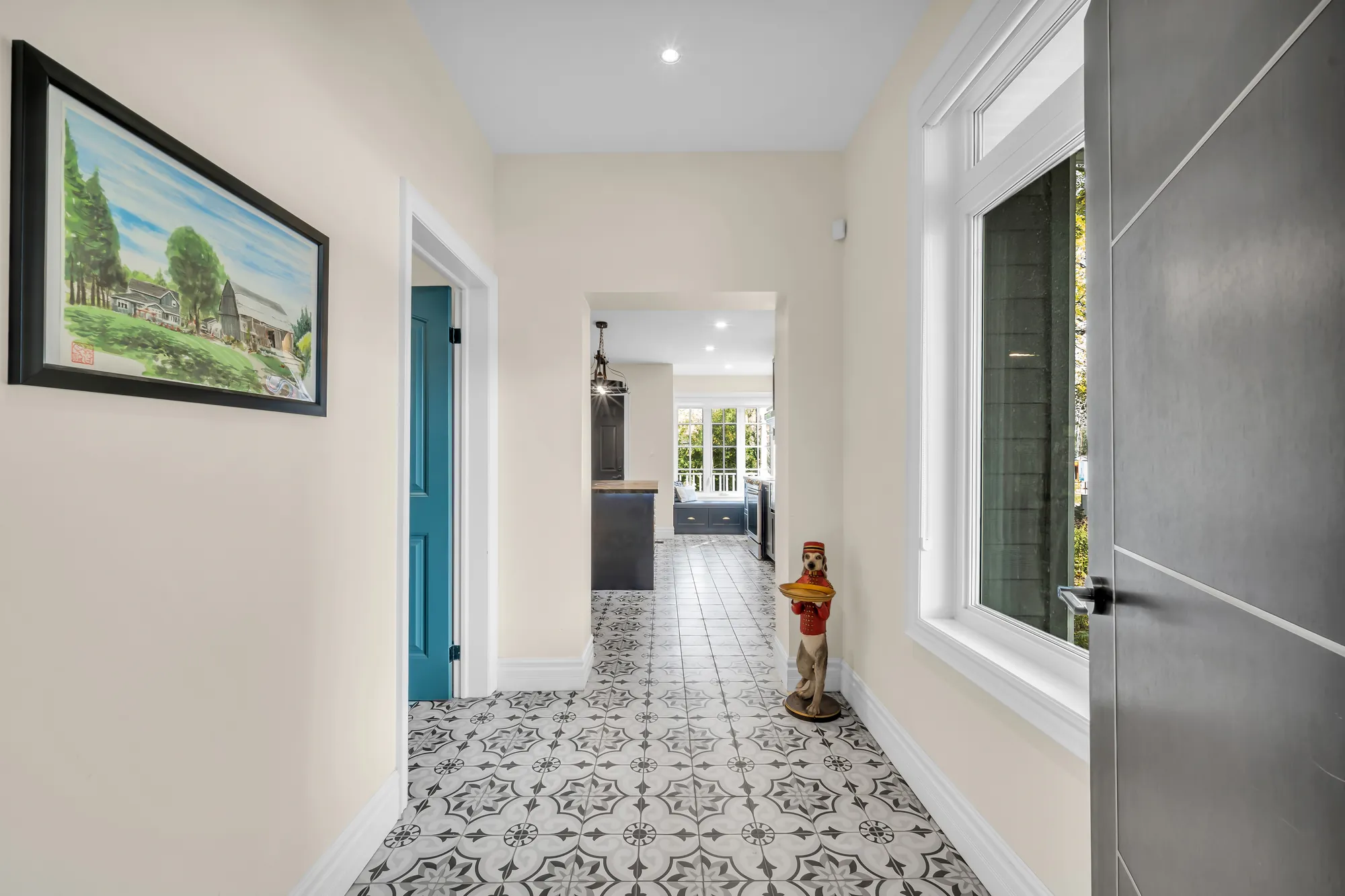 The hall into the east wing: patterned grey-and-white tile, a teal door, a statue, the kitchen at the far end