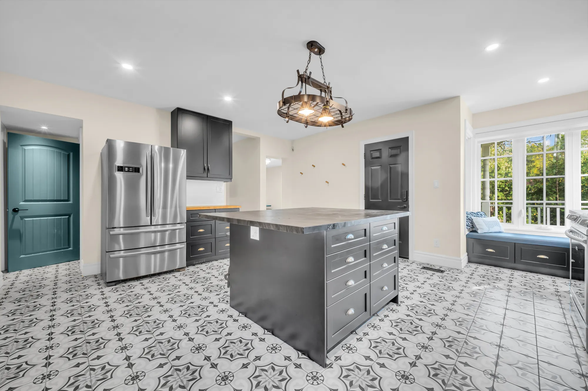 The eat-in kitchen: black cabinets, an island with a wood top, a stainless refrigerator, an iron chandelier, patterned tile, a window seat, a teal door