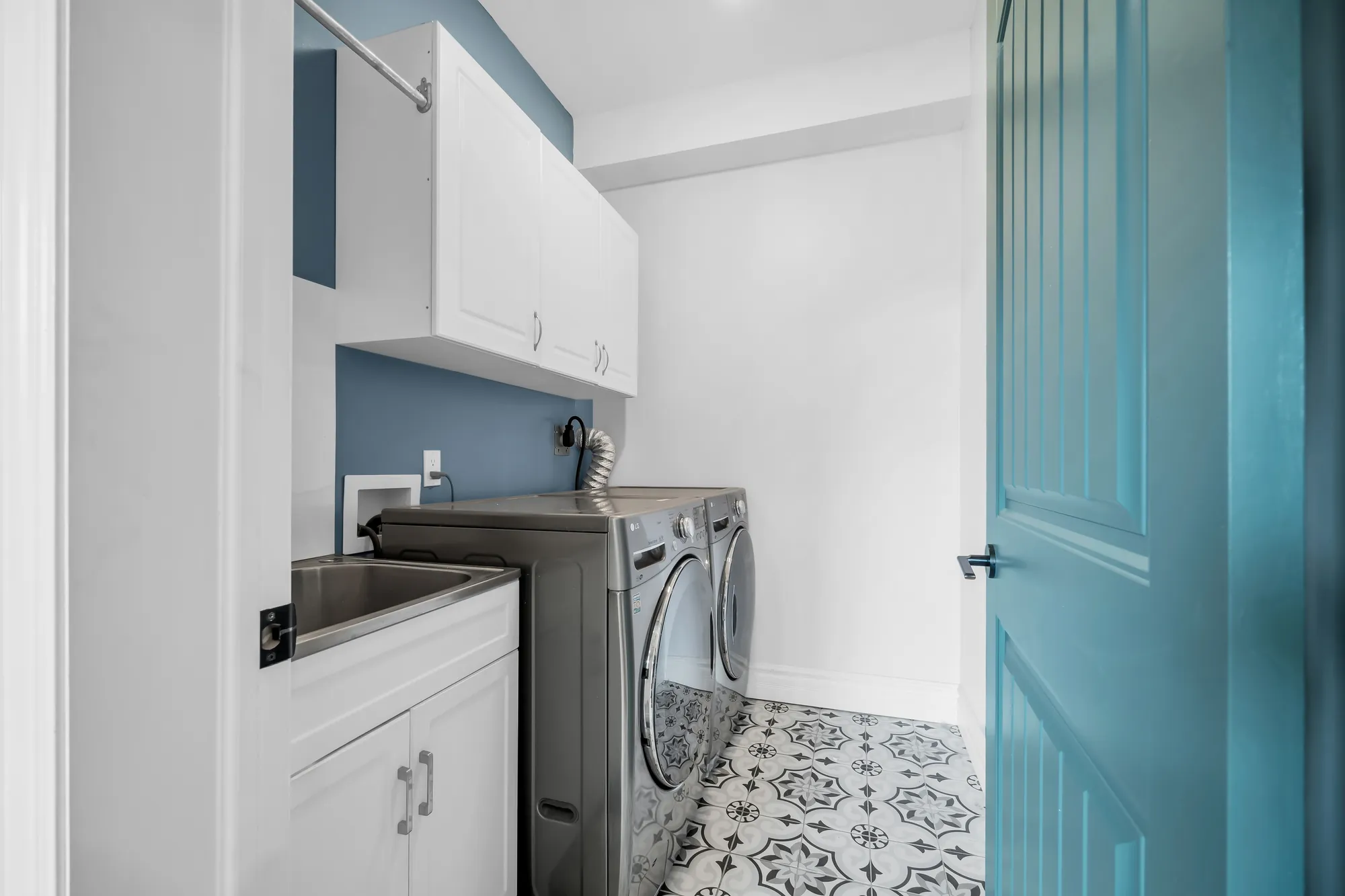A laundry: a washer and dryer, a sink and white cabinets, a teal door