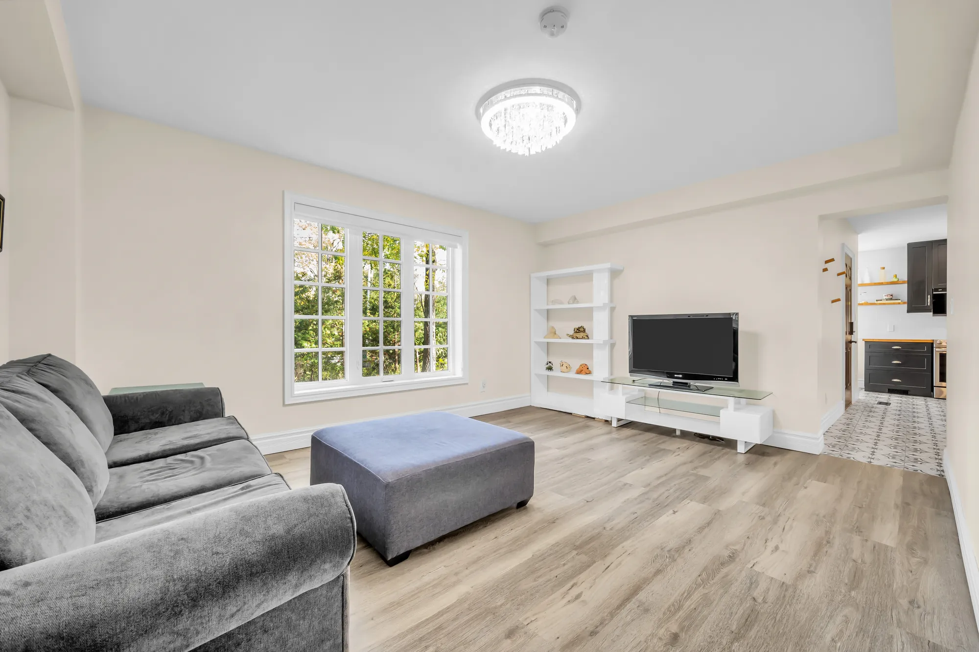 The same room toward a television and white shelves, the kitchen through the doorway