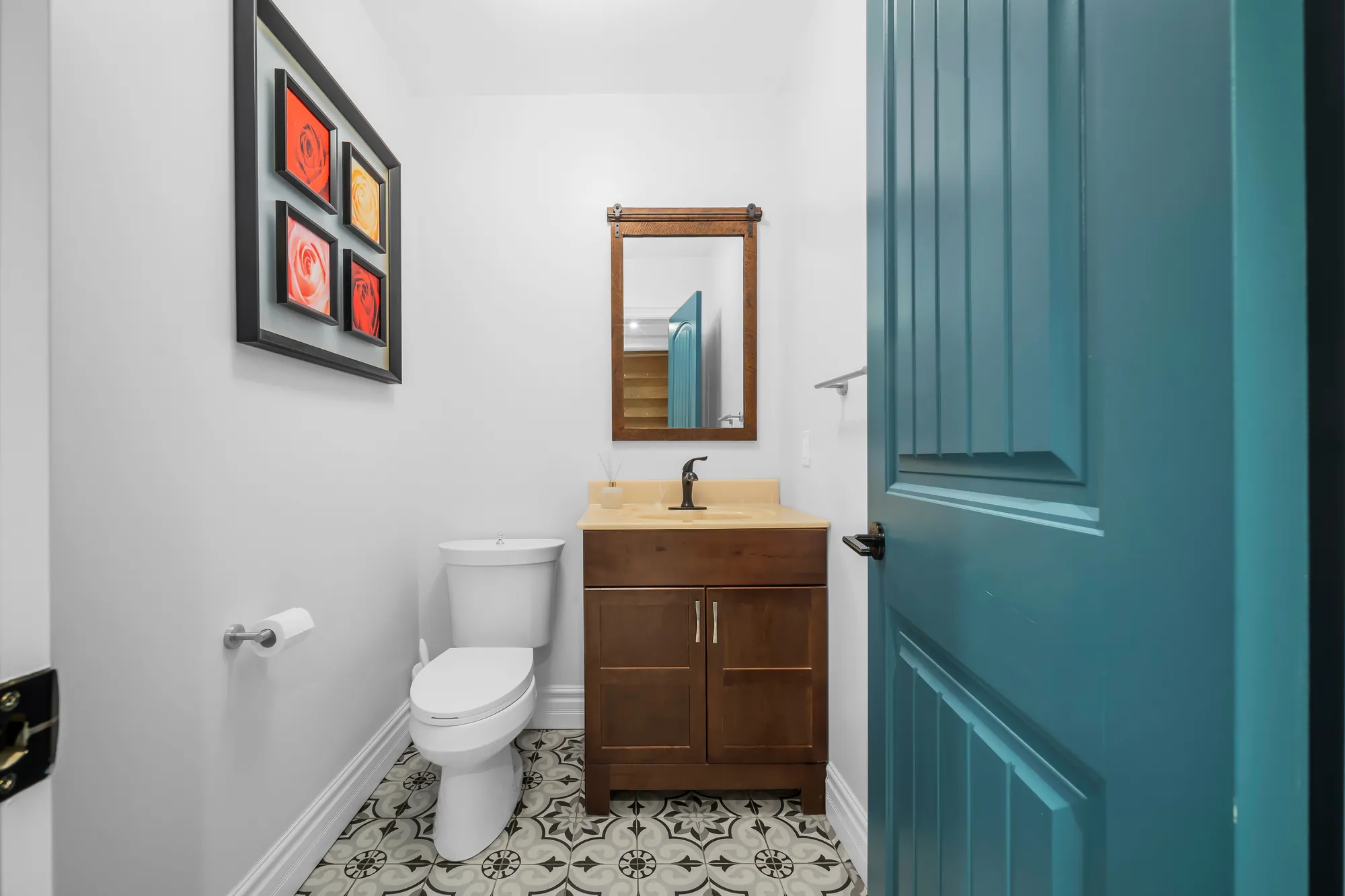 A powder room: a dark wood vanity, a toilet, patterned tile, a teal door