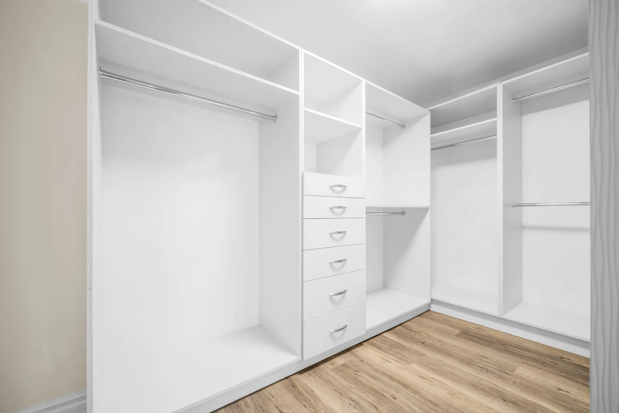 A walk-in closet with white built-in rails, shelves and drawers