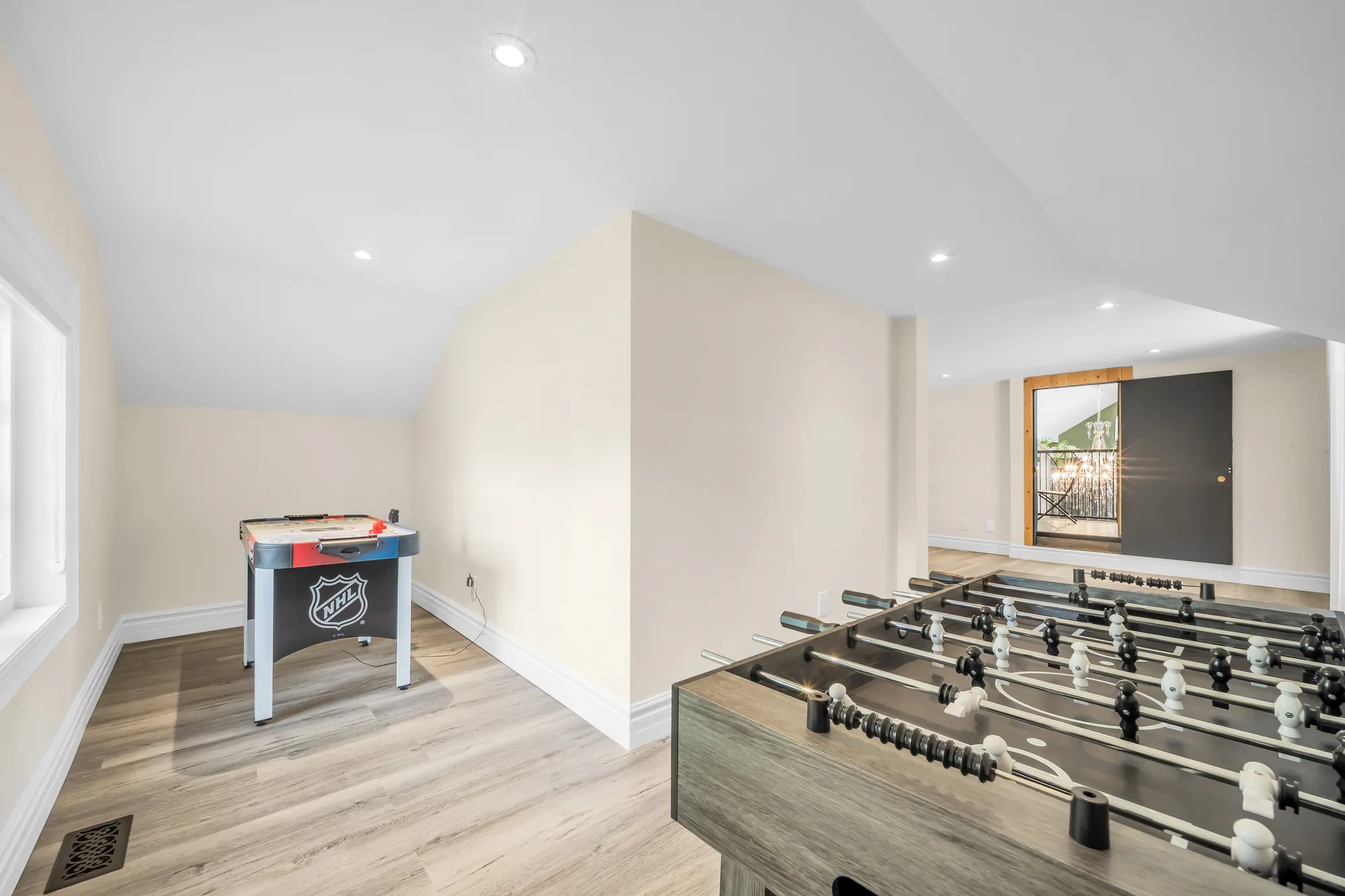 Under a sloped ceiling: a foosball table and an air hockey table, a window