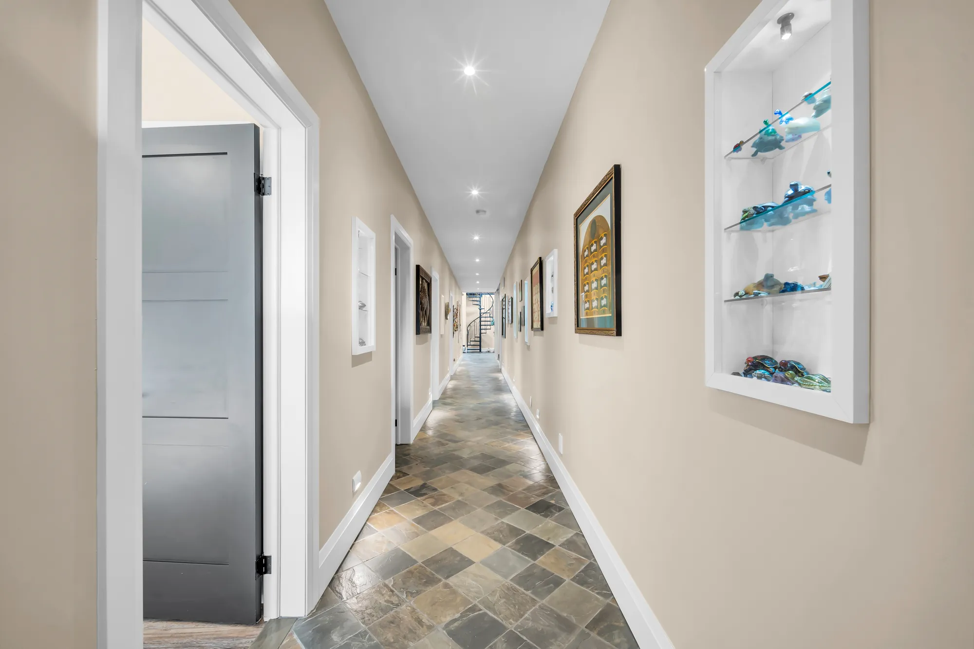 The long hall: a slate floor, a lit niche with glass art, doors along both sides, framed prints