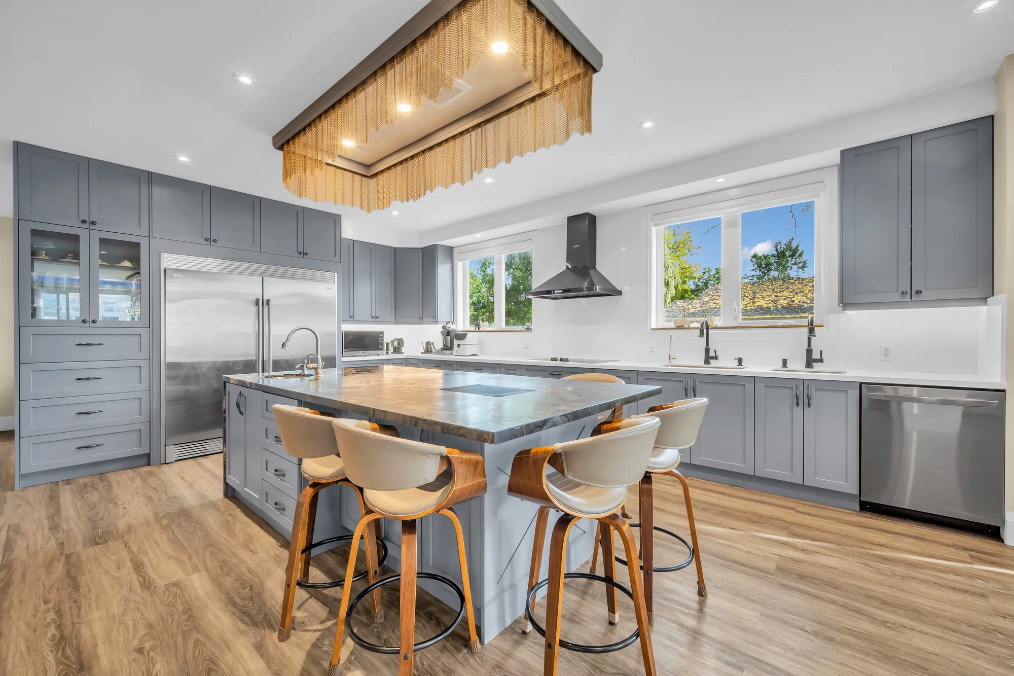 The island with four upholstered stools under a long light fixture, the cabinets and the refrigerators beyond