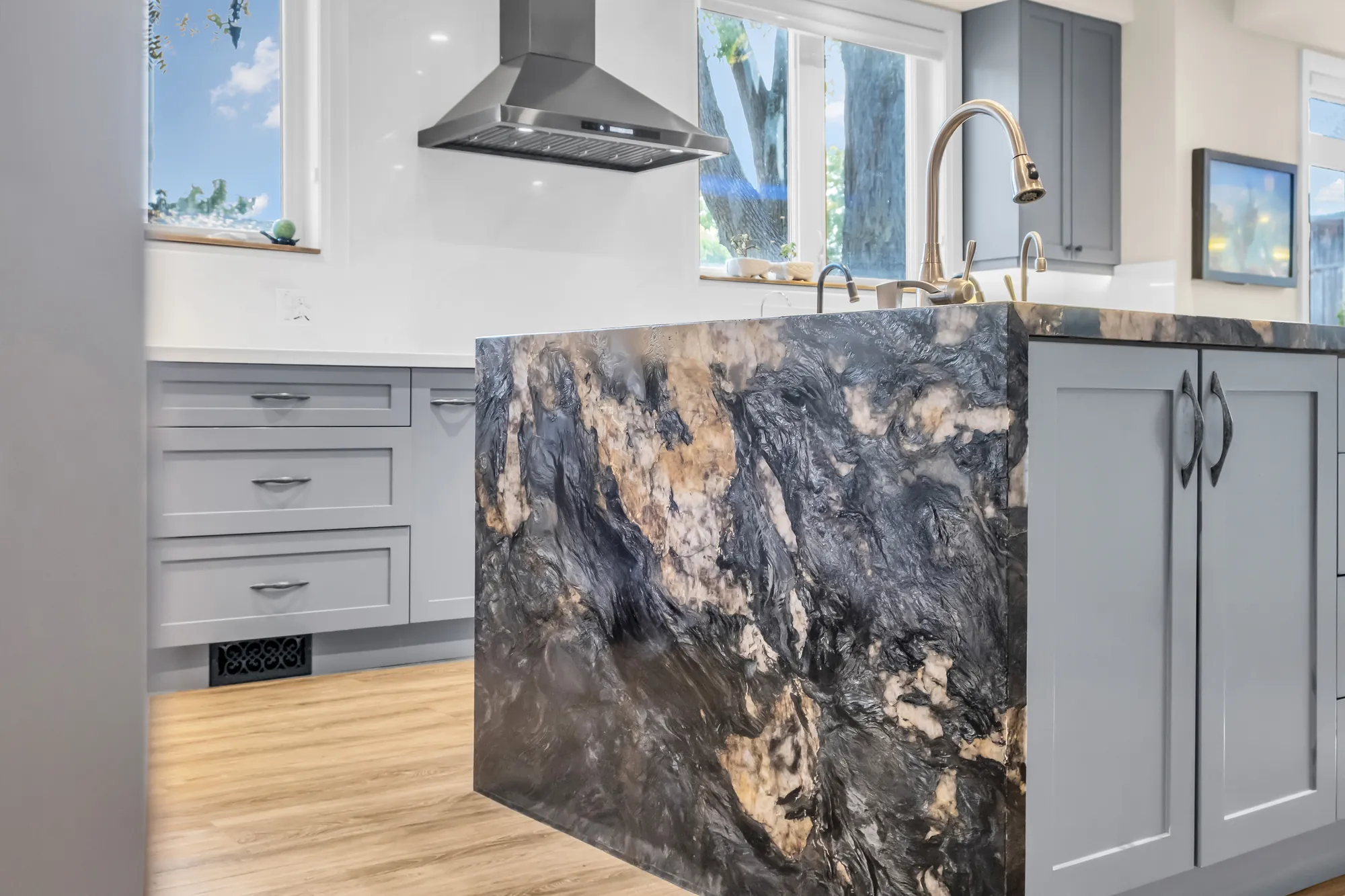 The end of the island: a waterfall edge in dark veined stone, grey cabinets, the hood beyond