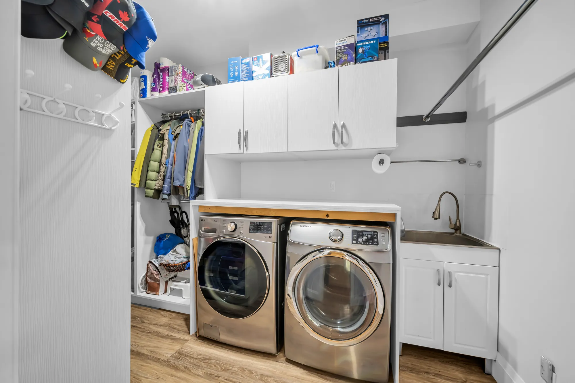 The laundry: a front-loading washer and dryer under a counter, white cabinets, a sink, hooks and shelves