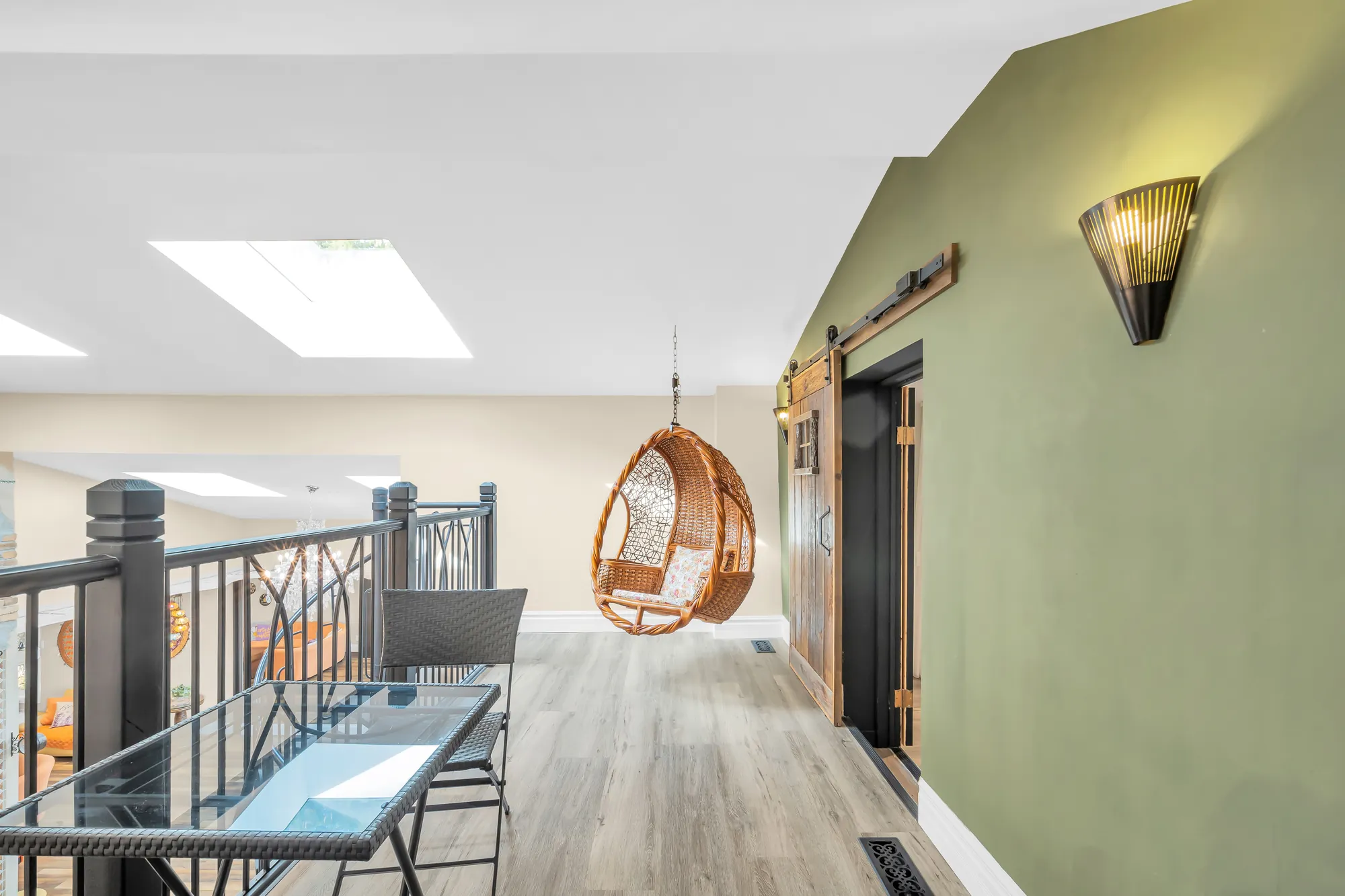 The loft: a hanging rattan chair, a glass table, a railing over the flex area, a green wall, a sliding barn door