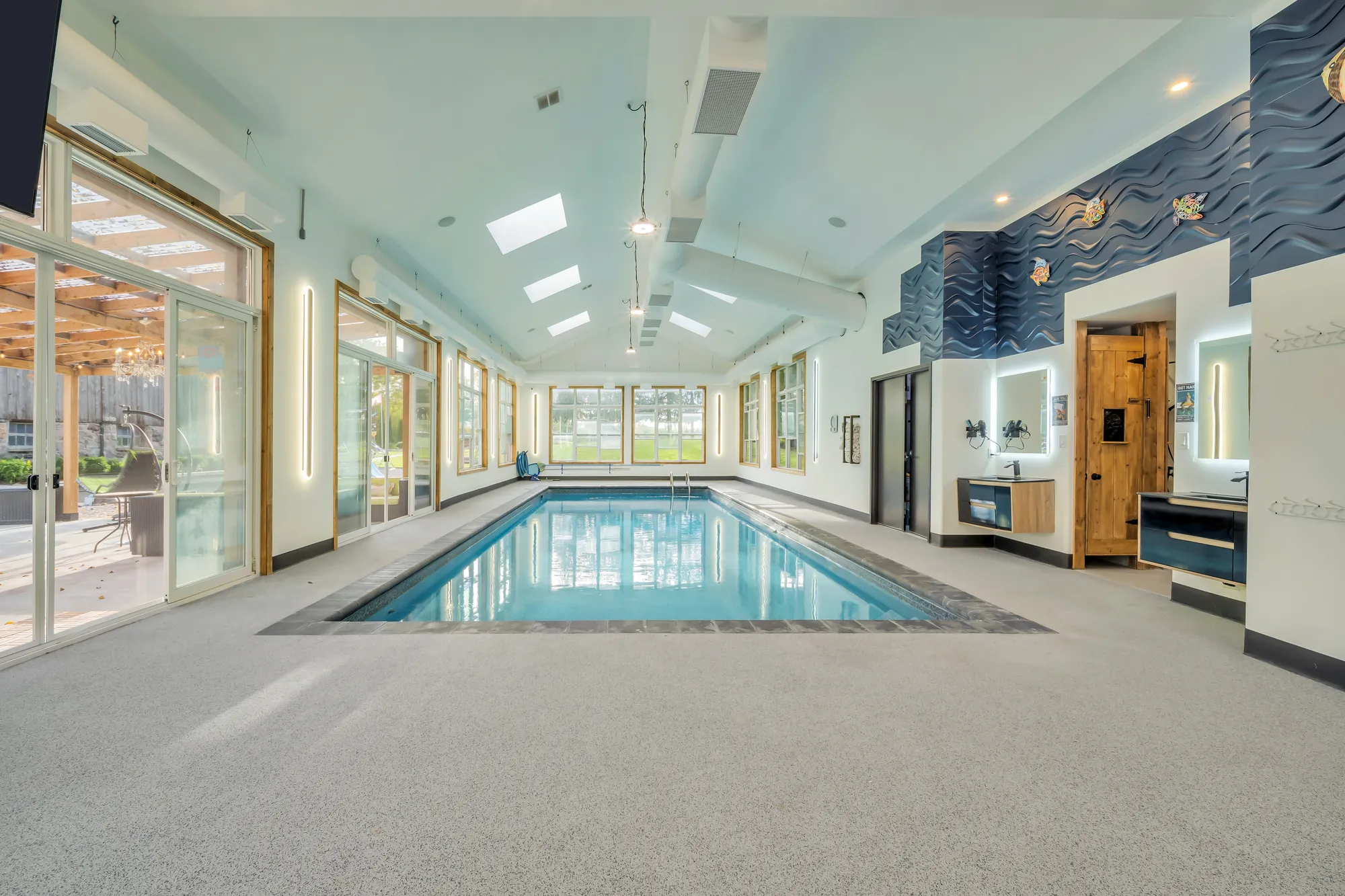 The pool from one end: glass doors along one side, a wooden door and a dark blue panel on the far wall