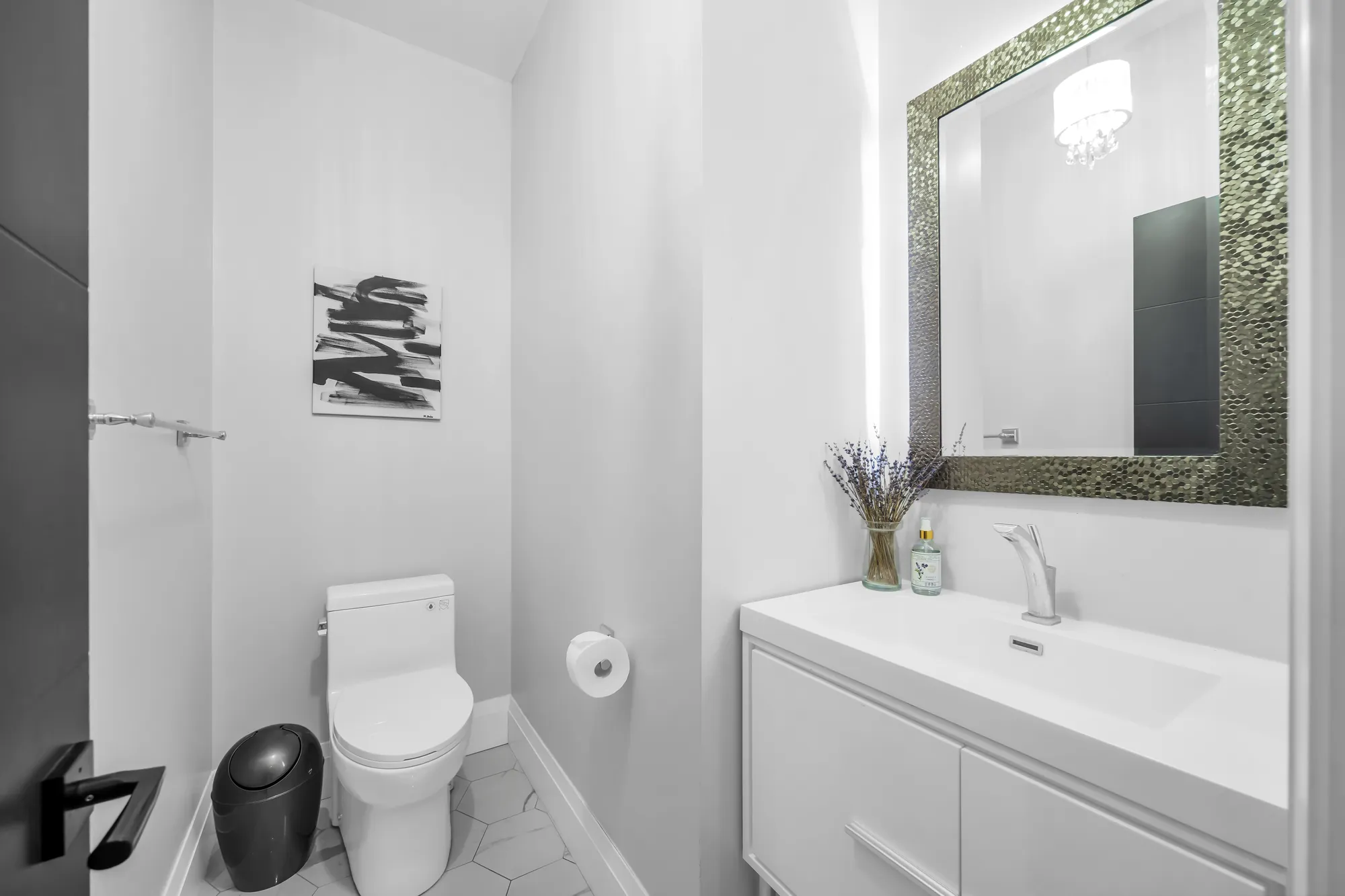 A powder room: a wall-hung white vanity, a mirror framed in mosaic, a toilet