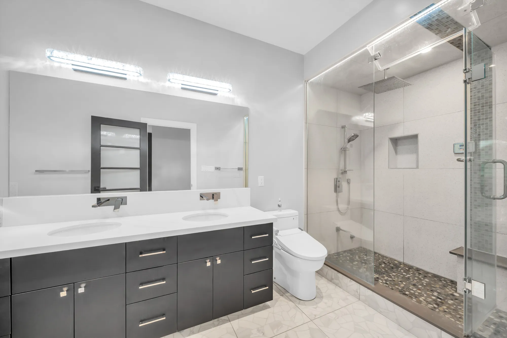 The double vanity and a glass-enclosed shower with a pebble floor and a rain head
