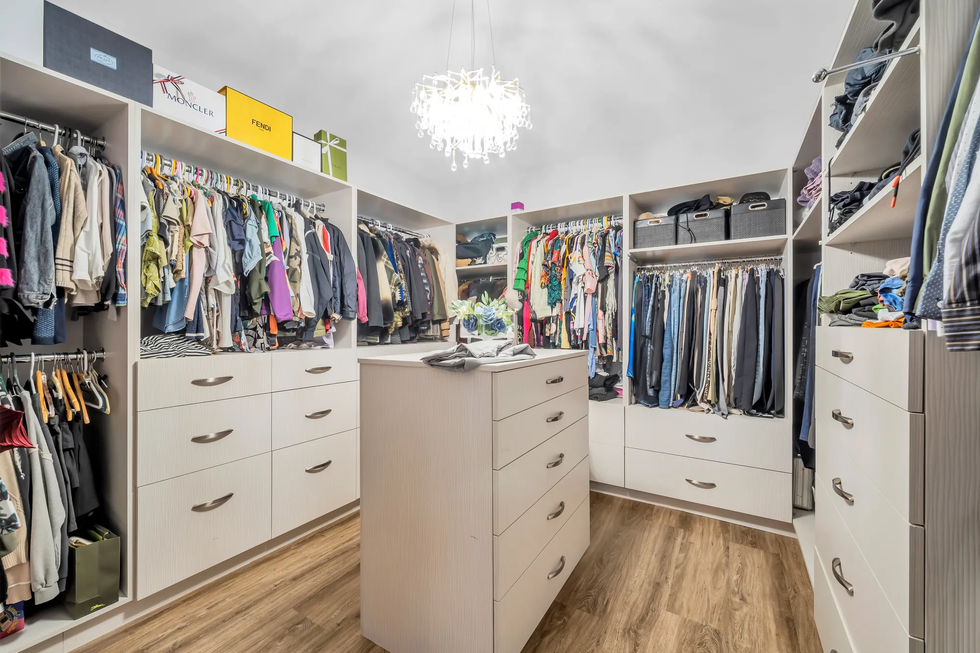 The walk-in closet: built-in hanging rails and shelves on three sides, an island of drawers, a crystal chandelier