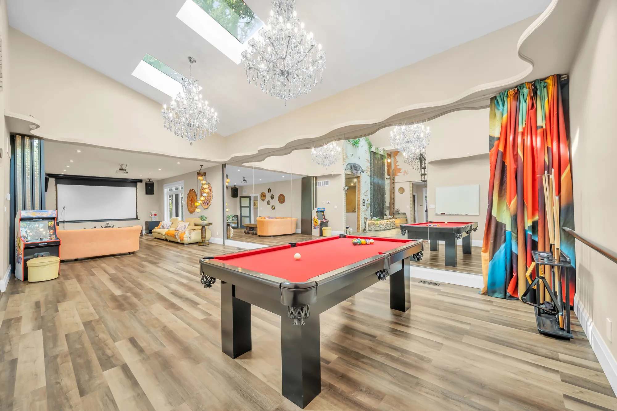 A pool table, a screen and seating at the far end of the recreation room, crystal chandeliers