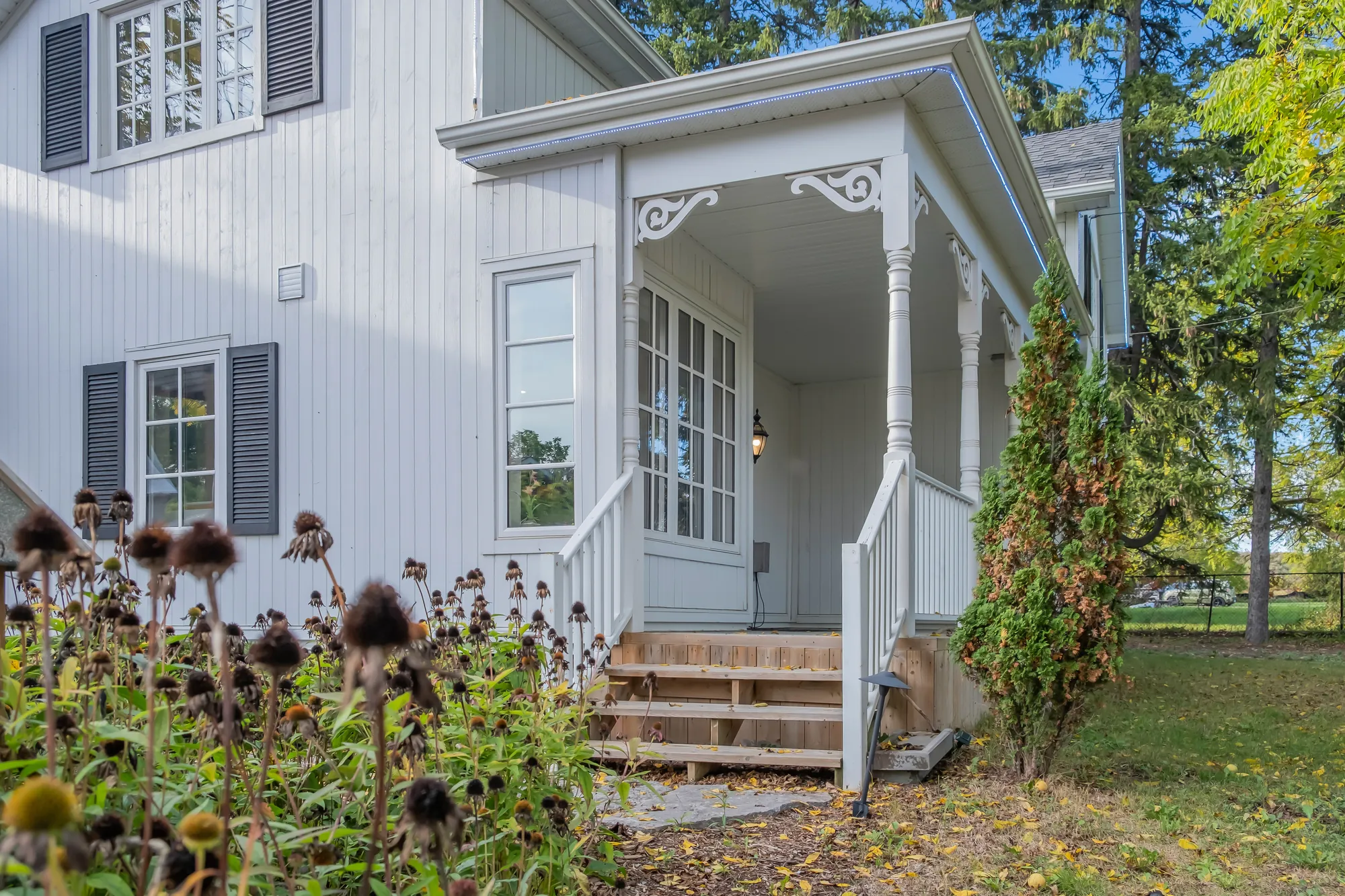 The white wing&rsquo;s porch: turned posts and white fretwork brackets, wooden steps, French doors, coneflowers in the foreground