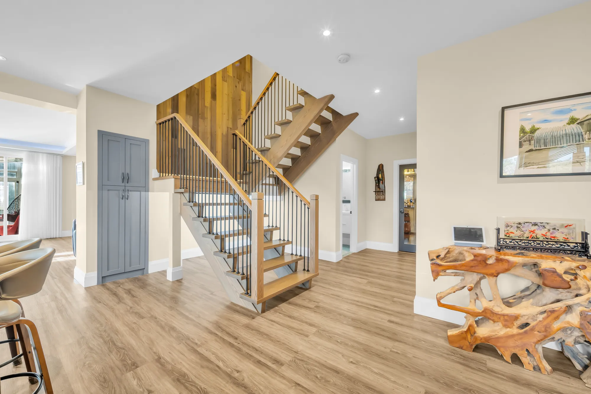 The stair to the upper floor in wood with black balusters, a root-wood table, the living area