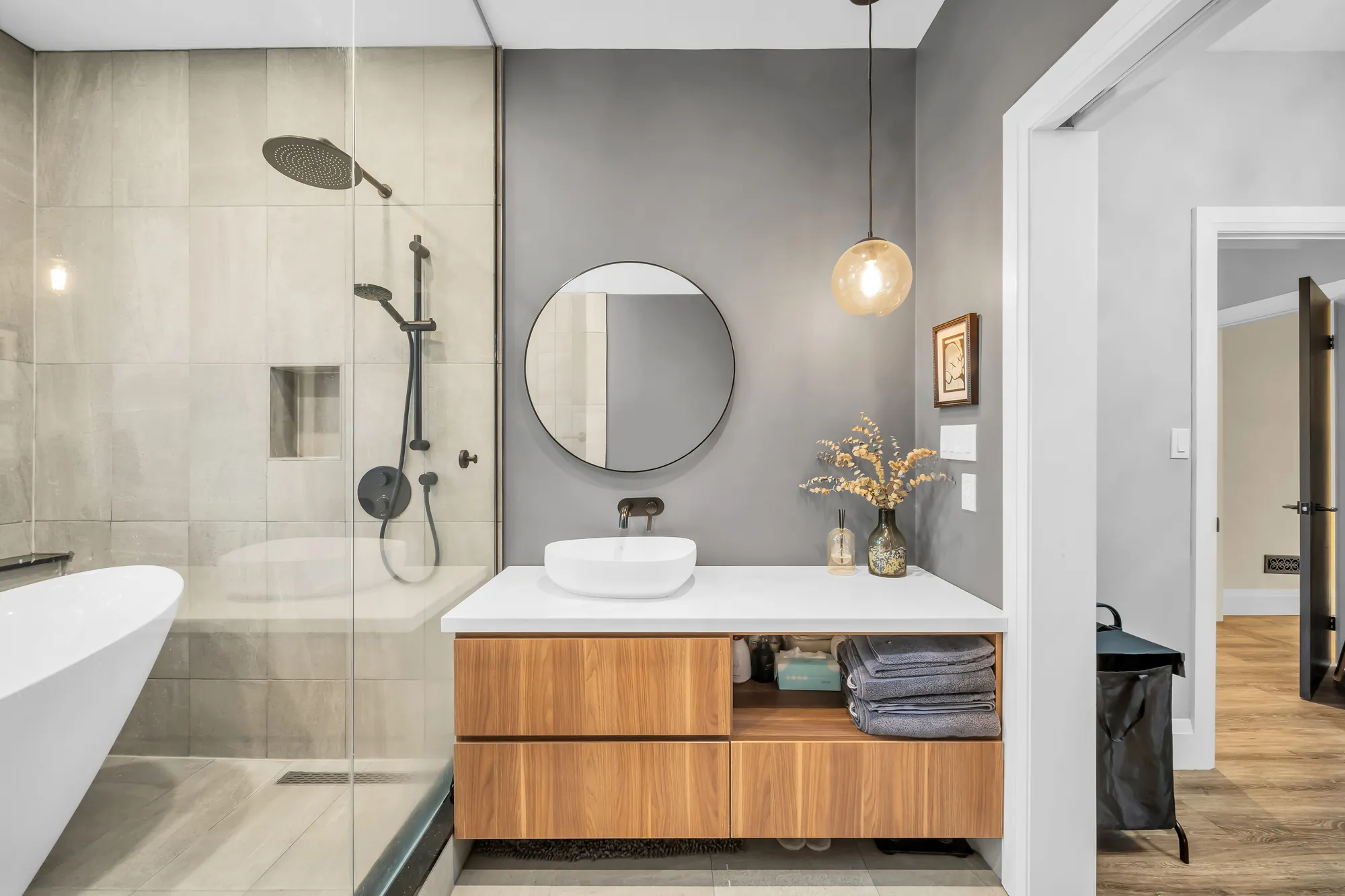 The same bathroom: a glass shower with a black rain head, the wood vanity