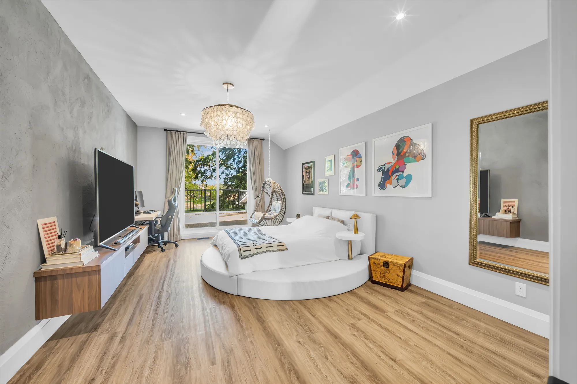 The same bedroom toward sliding glass doors to a balcony: the round bed, a television on a low cabinet, a desk, a hanging chair