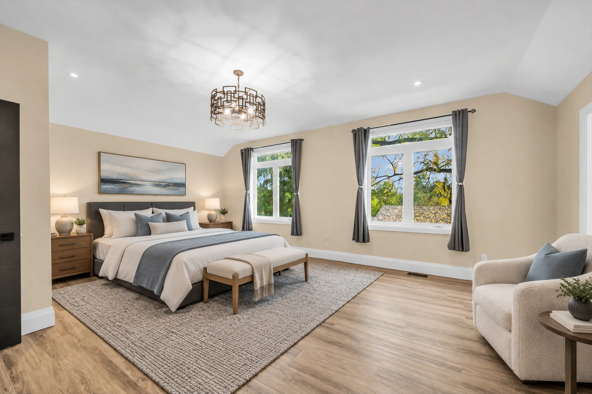 A bedroom under a sloped ceiling, virtually staged: an upholstered bed with a bench, night tables and lamps, a rug, an armchair, a seascape print; two windows with grey curtains, a geometric chandelier