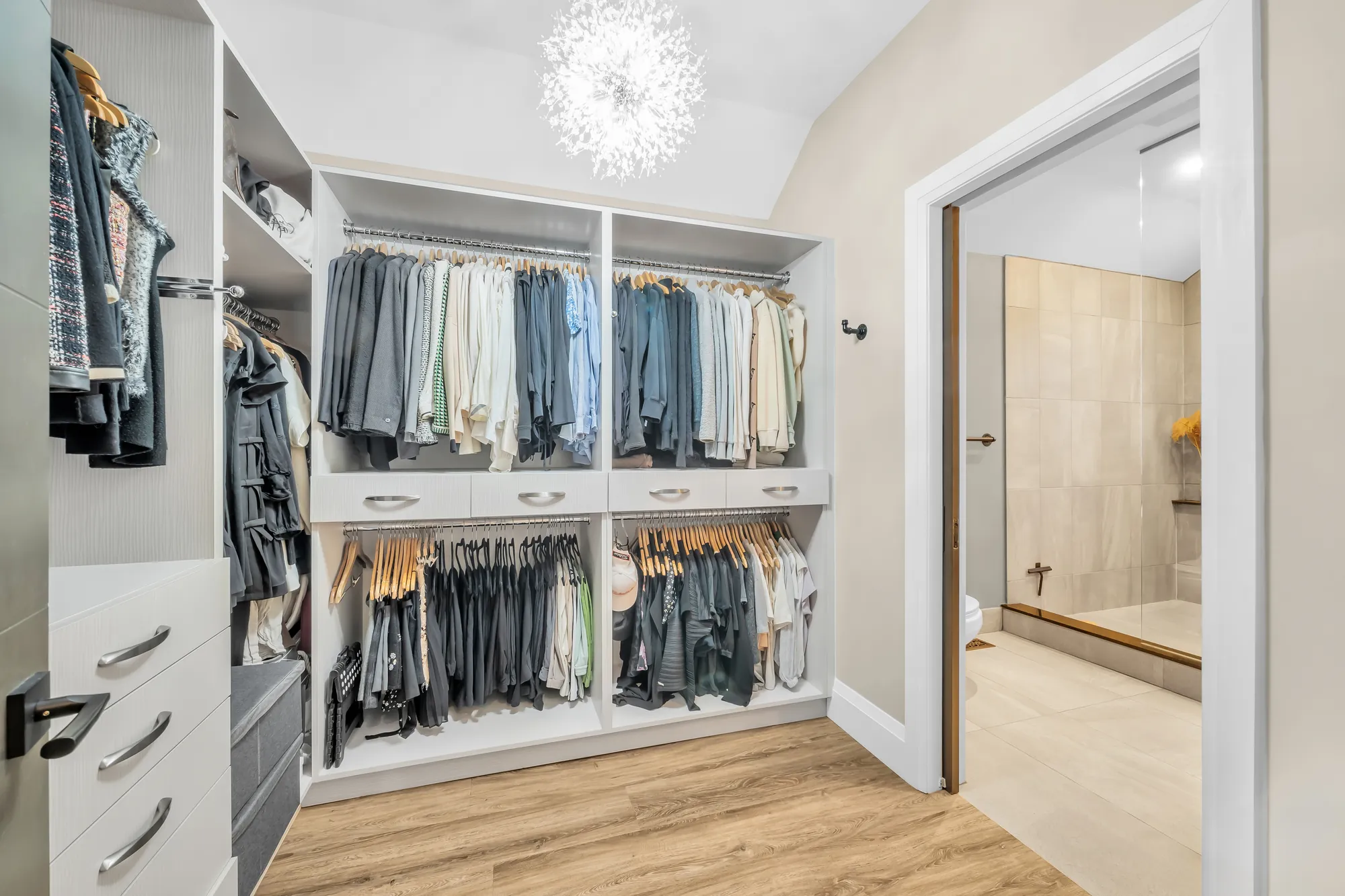 A walk-in closet with built-in rails and drawers, a doorway to the bathroom