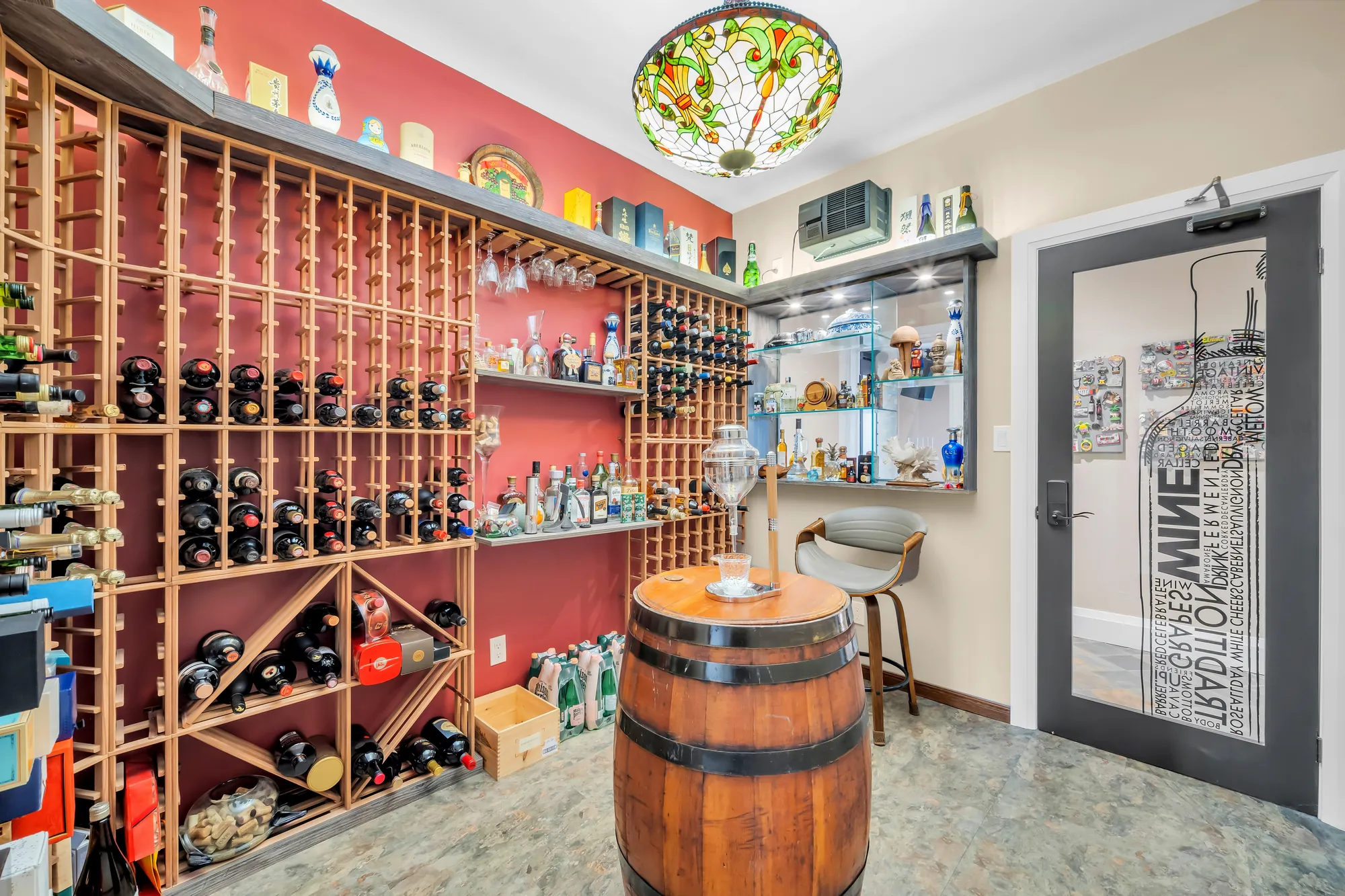 The wine room: floor-to-ceiling wood racks on a red wall, a wine-barrel table, a stained-glass ceiling light, a glass door